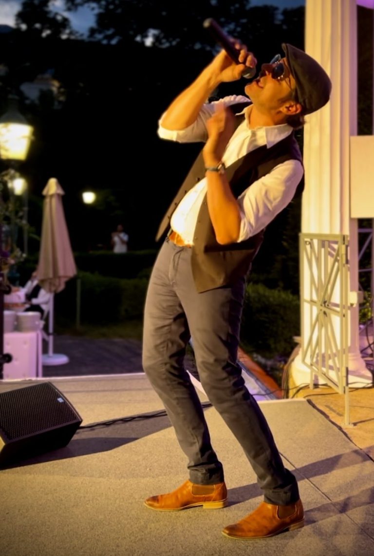 Italienischer Sänger buchen Italienischer Sänger mit Mikrofon, in eleganter Kleidung, während er auf einer Bühne singt.