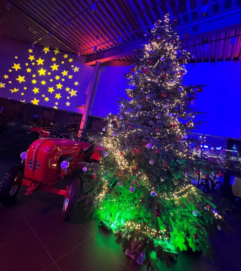 Weihnachtsbaum mit bunten Lichtern und rotem Traktor im Hintergrund.