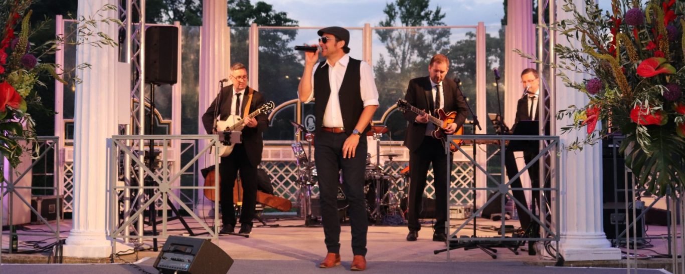 Live Band Österreich Sänger auf einer Bühne, umgeben von Instrumentalisten.