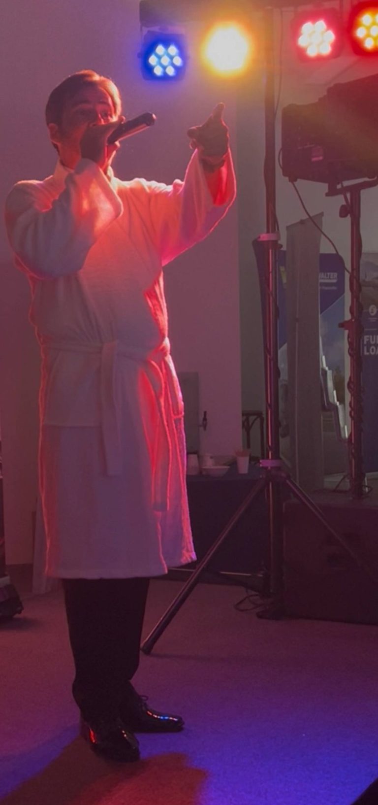 Udo Jürgens Sänger steht im Bademantel Outfit auf Bühne und wird von einer farbintensiven Beleuchtung angestrahlt