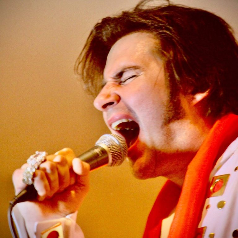 Elvis Imitator buchen Sänger als Elvis Imitator im Elvis-Kostüm, der leidenschaftlich ins Mikrofon singt.