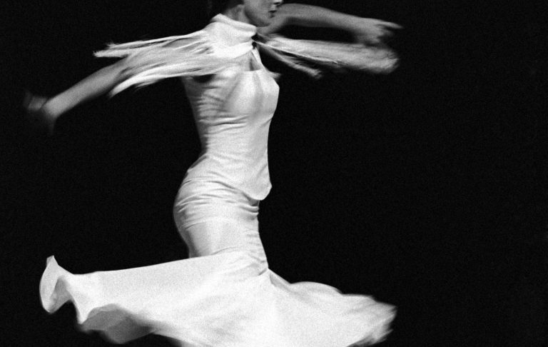 Eine Frau in einem weißen Kleid, die sich tänzerisch dreht.