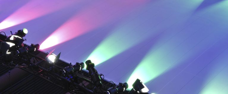 Bunte Lichtstrahlen auf einer Bühne in Lila, Pink und Blau auf einer weißen Fläche.