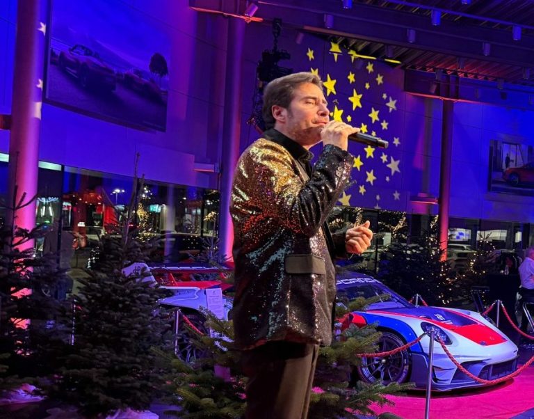 Sänger für Schlagerparty Mann singt auf einer Bühne in einem Autohaus, umgeben von Weihnachtsbaum-Dekoration.