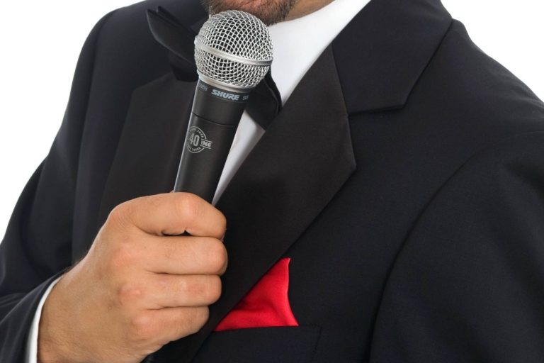 Mann in Smoking mit rotem Stecktuch hält ein Mikrofon.