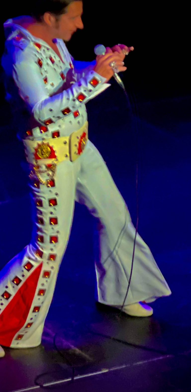 Elvis Double buchen Ein Elvis Cover Sänger in einem glitzernden weißen Anzug mit roten Akzenten und Mikrofon auf der Bühne.