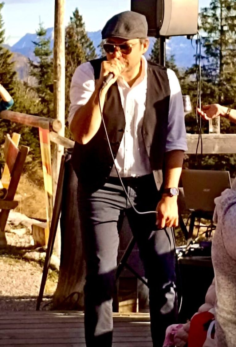 Österreichischer Sänger Mann mit Sonnenbrille und Hut singt auf einer Bühne im Freien.