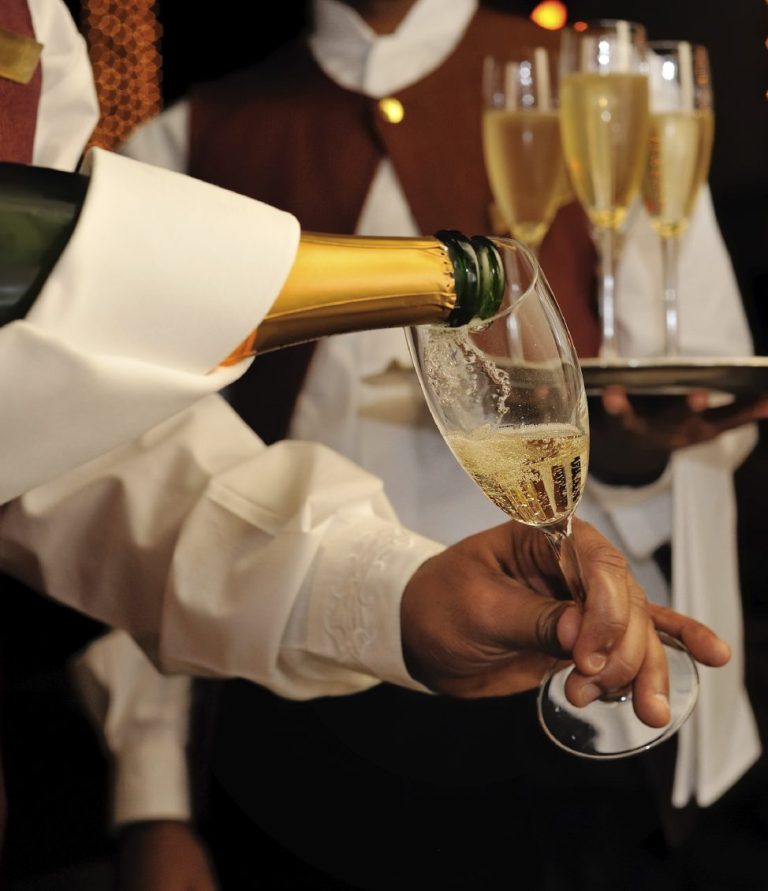 Ein Kellner gießt Champagner in ein Glas, während ein Tablett mit Gläsern bereitsteht.