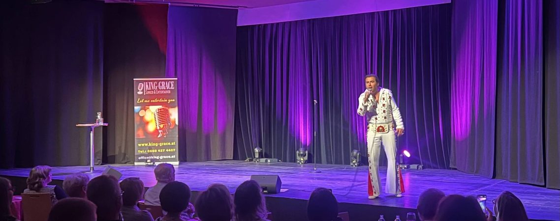 Elvis Showeinlage Firmenfeier Ein Elvis Imitator auf der Bühne, der eine Performance vor einem Publikum präsentiert.