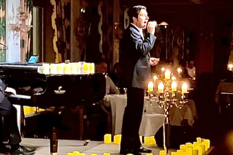 Ein Entertainer steht im Smoking auf einer Bühne mit Klavier