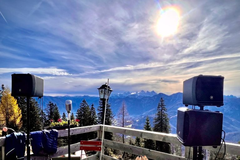 Aussicht auf Berge mit Lautsprechern und Sonne am Himmel, umgeben von Bäumen.